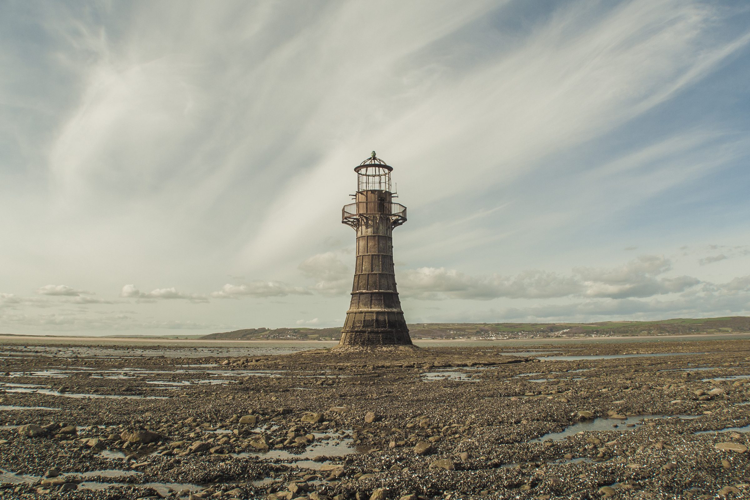 A lighthouse standing alone on a flat shore under a wide sky